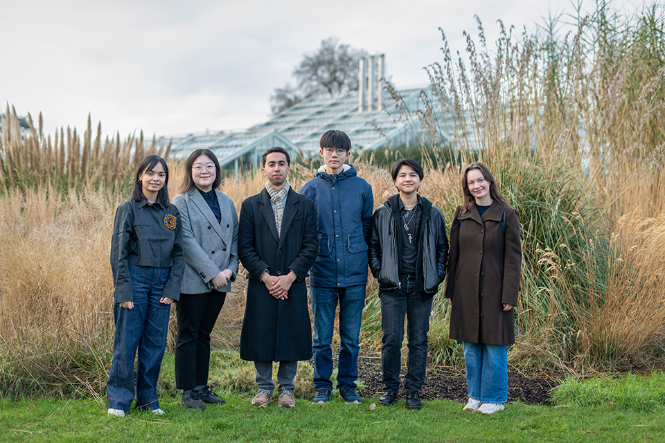 Six students, wrapped in warm clothes, standing in front of plants test
